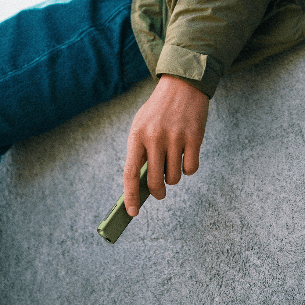 En person, der holder en mosgrøn IQOS ILUMA ONE