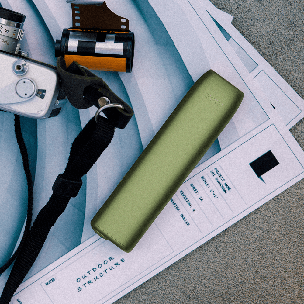 	En IQOS ILUMA ONE ved siden af et kamera