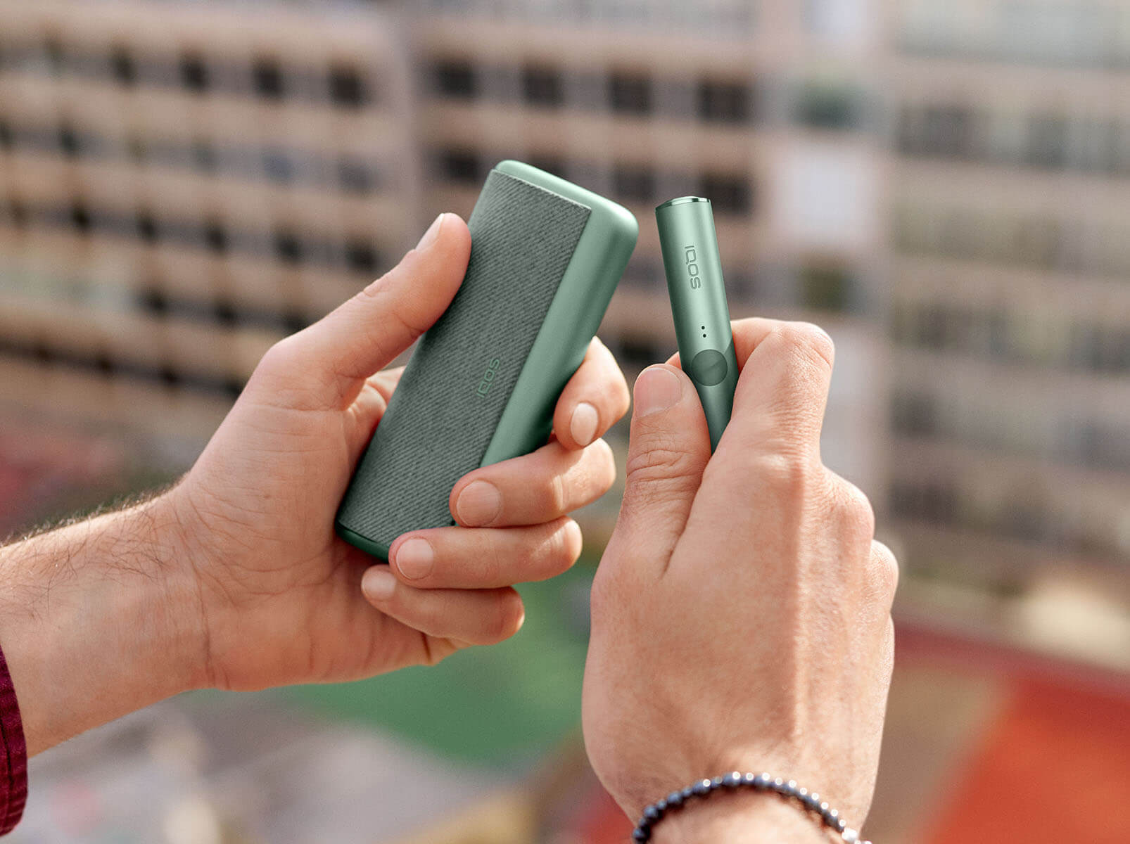 A person holding a moss green IQOS ILUMA PRIME