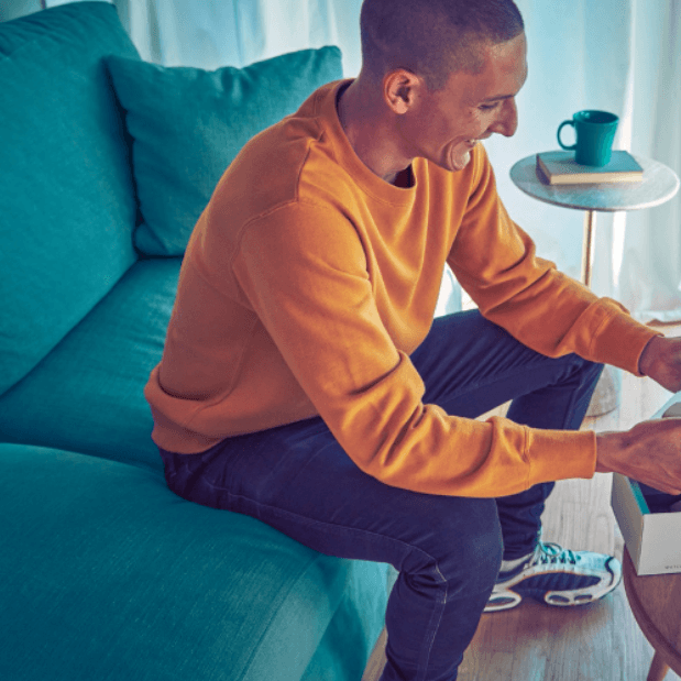 smiling man sitting on a couch opening a box