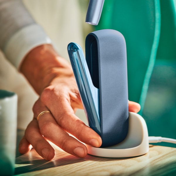 A person placing an IQOS ILUMA Pocket Charger into a charging station.